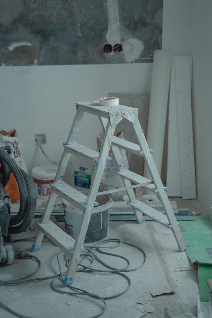 brand-02 A metal ladder stands amidst renovation supplies including paints and plaster in an indoor setting.