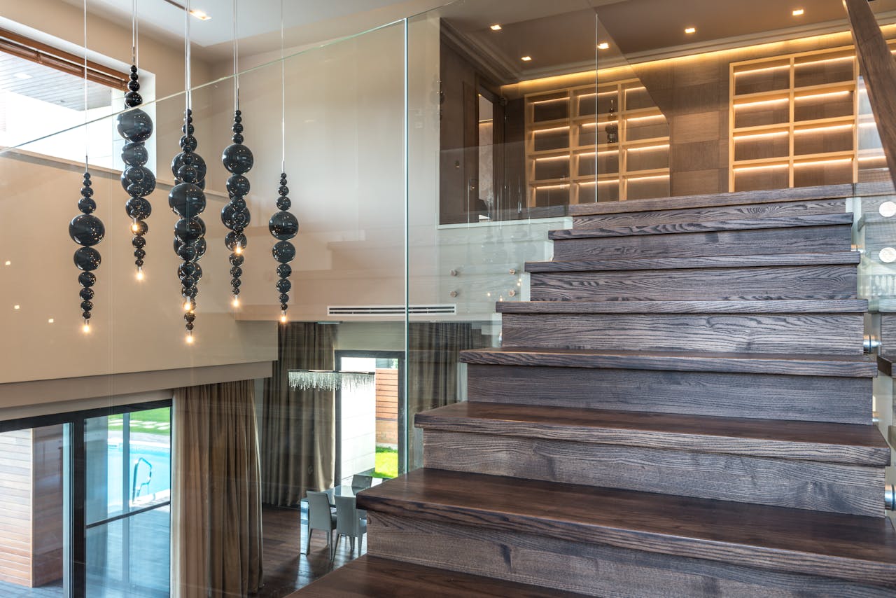 brand-03 Elegant interior design featuring a wooden staircase with glass railing and artistic lighting.